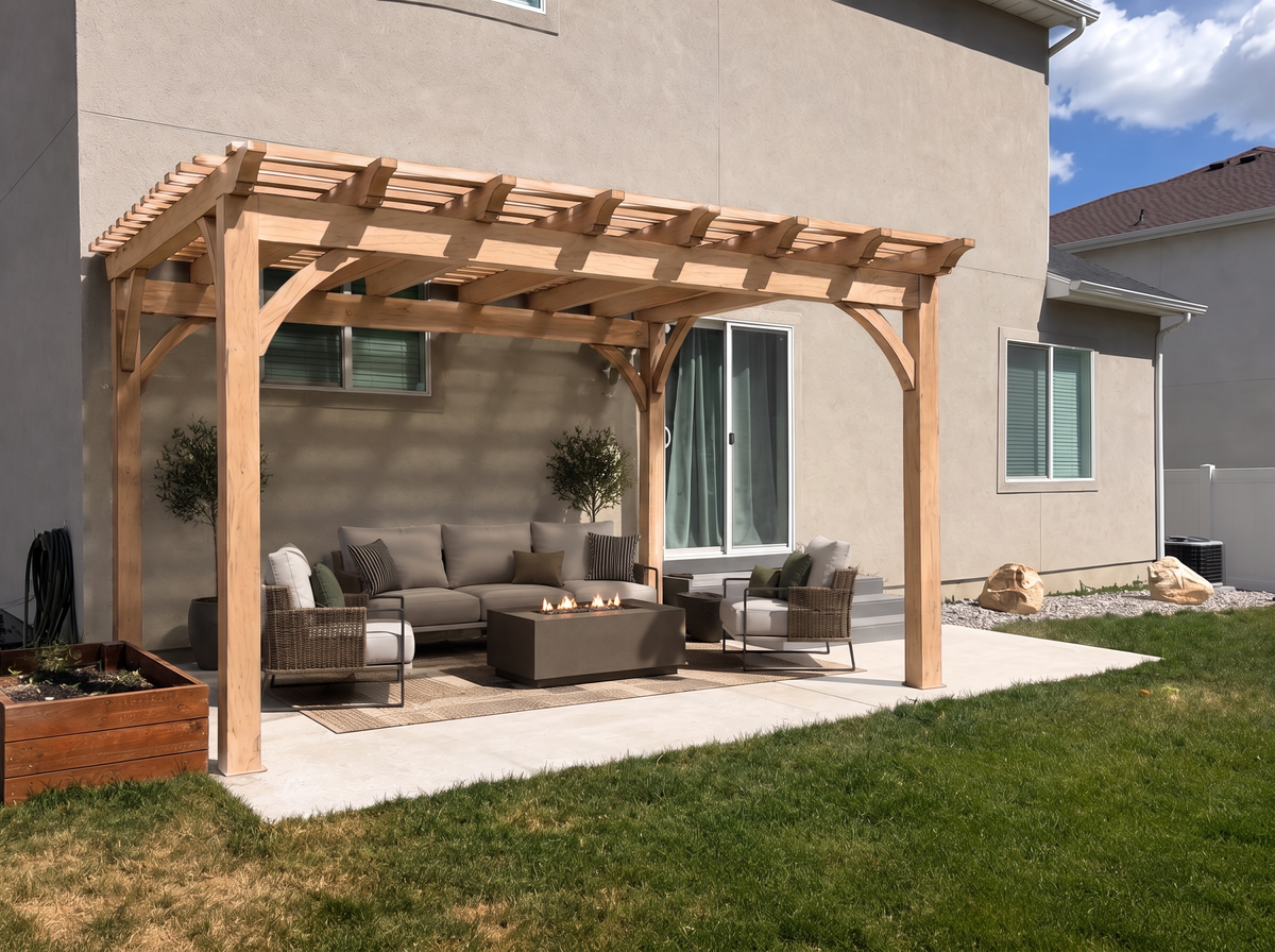 A custom Douglas fir pergola attached to the back of a home, with curved braces sheltering a sofa and fire table on a concrete patio.