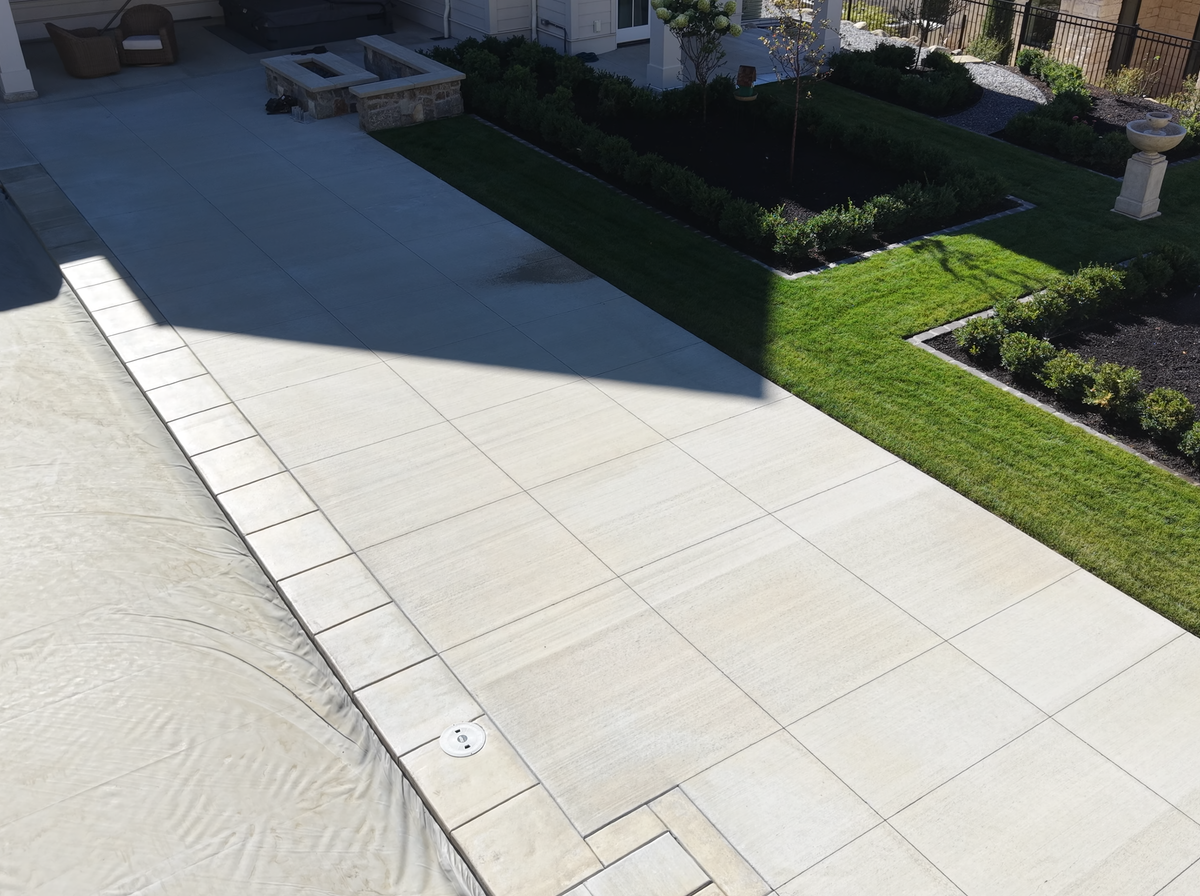 The bare concrete pool deck and garden beds of an Alpine, Utah backyard before the pergola went in