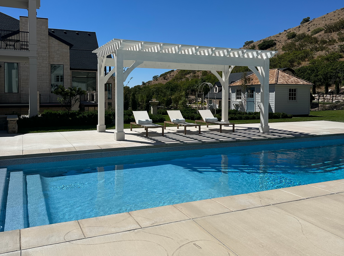 Pinto White 12×20 pergola across the pool in Alpine, Utah, loungers underneath and the hillside behind