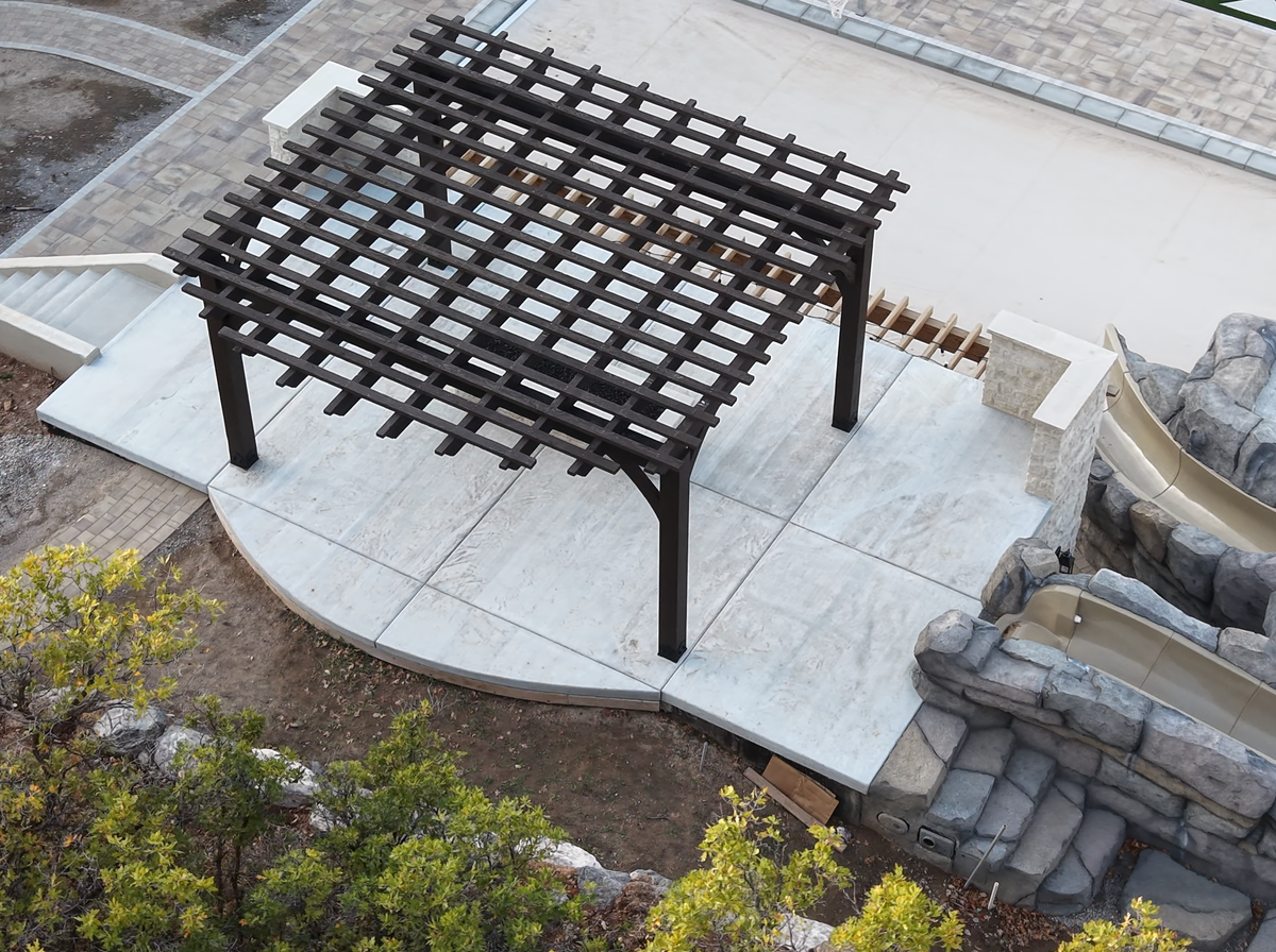 Aerial three-quarter view of the Cordovan Brown 18×18 pergola on the roof deck over a covered pool in Elk Ridge, Utah