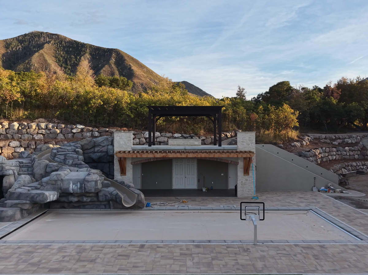 The stone-walled covered pool in Elk Ridge, Utah, with the Cordovan Brown 18×18 pergola on its roof deck and the mountain behind