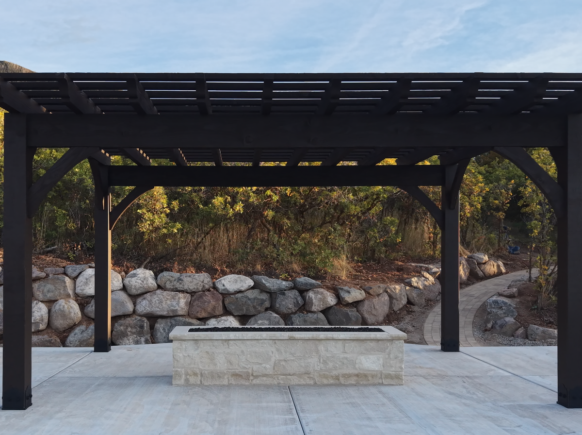 Cordovan Brown 18×18 timber pergola with curved knee braces on the roof deck over a covered pool in Elk Ridge, Utah
