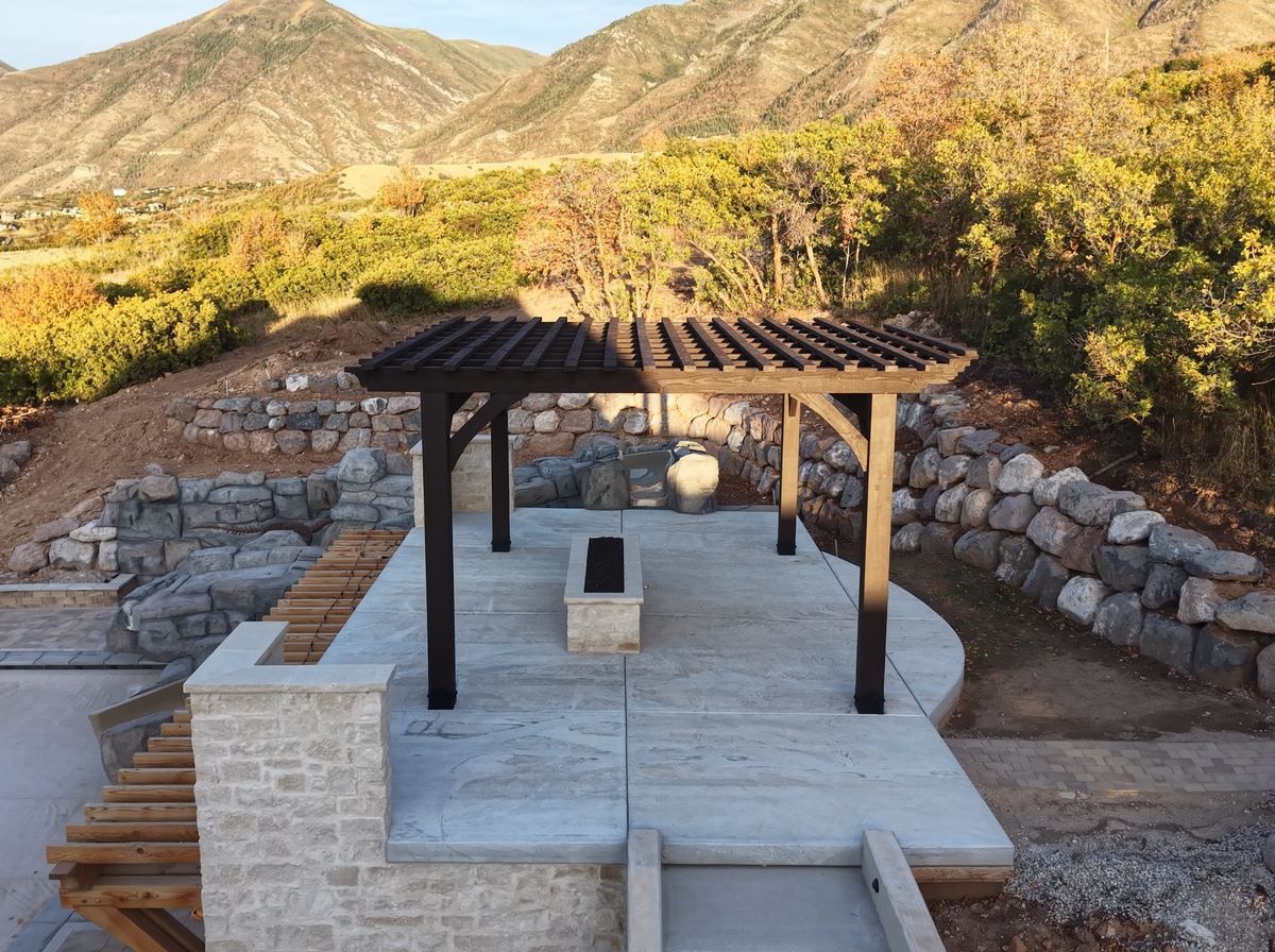 Cordovan Brown 18×18 timber pergola on the stone roof deck of a covered pool in Elk Ridge, Utah, with the mountains behind